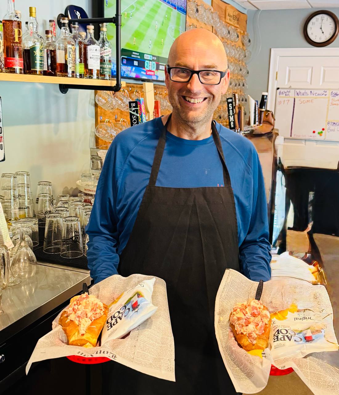 Dave, owner of Dave's Maine Café, holding two fresh lobster rolls at the bar